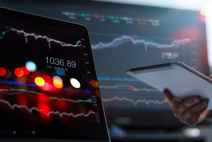 Laptop and tablet displaying financial market charts and trading data on digital screens.