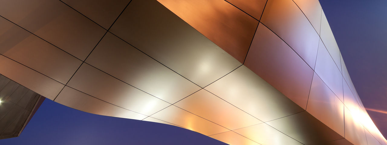 Close-up of a modern building facade with curved metallic panels reflecting warm light.