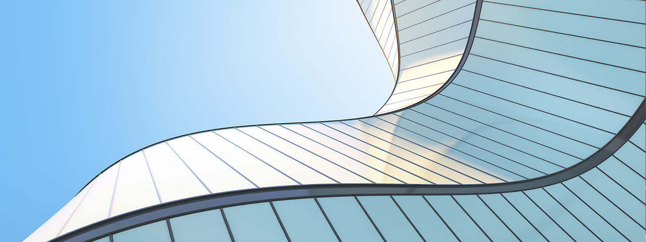 Curved glass and metal facade of a modern office building viewed from below against a clear blue sky.